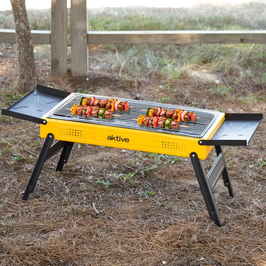 Barbacoa de carbón plegable Aktive 89x33x33 cm con bandejas laterales: en uso durante una barbacoa