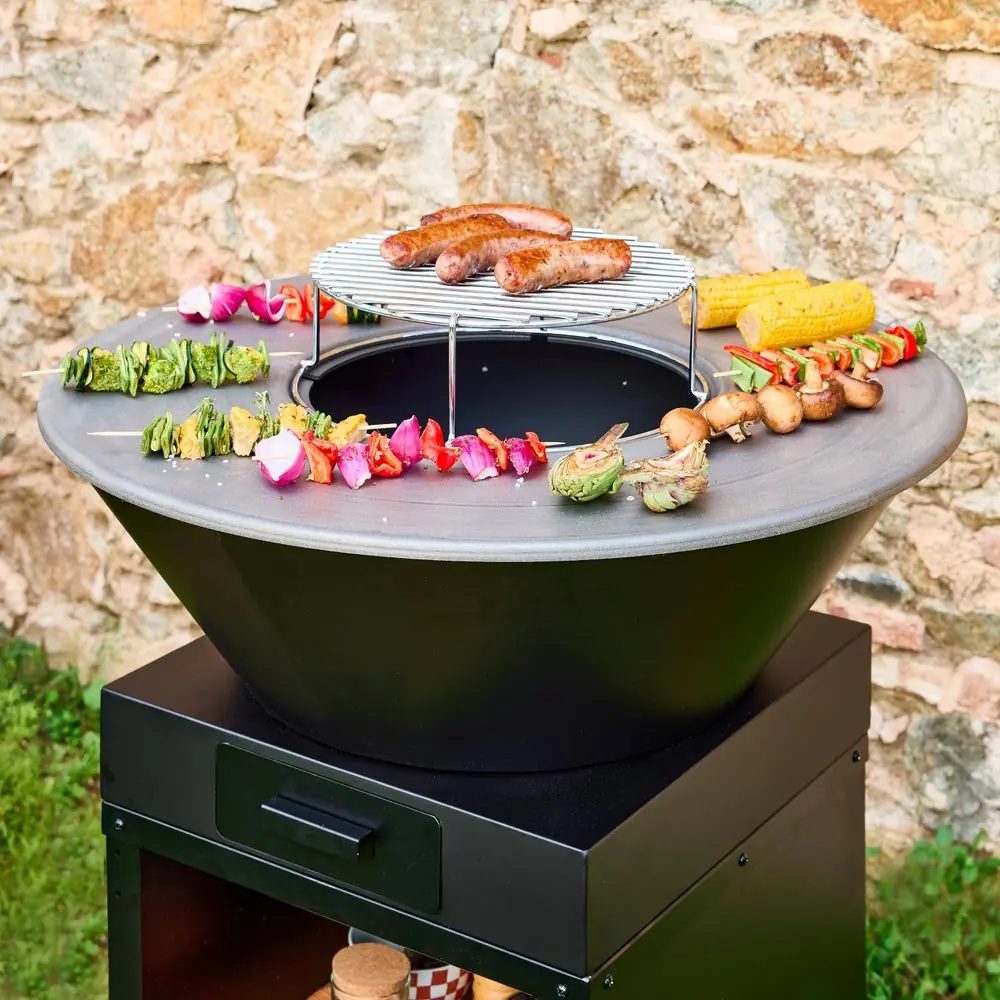Brasero barbacoa Mombacho Ø 81,5 cm con plancha y mueble para leña: la plancha de cocción cargada de brochetas, verduras y salchichas
