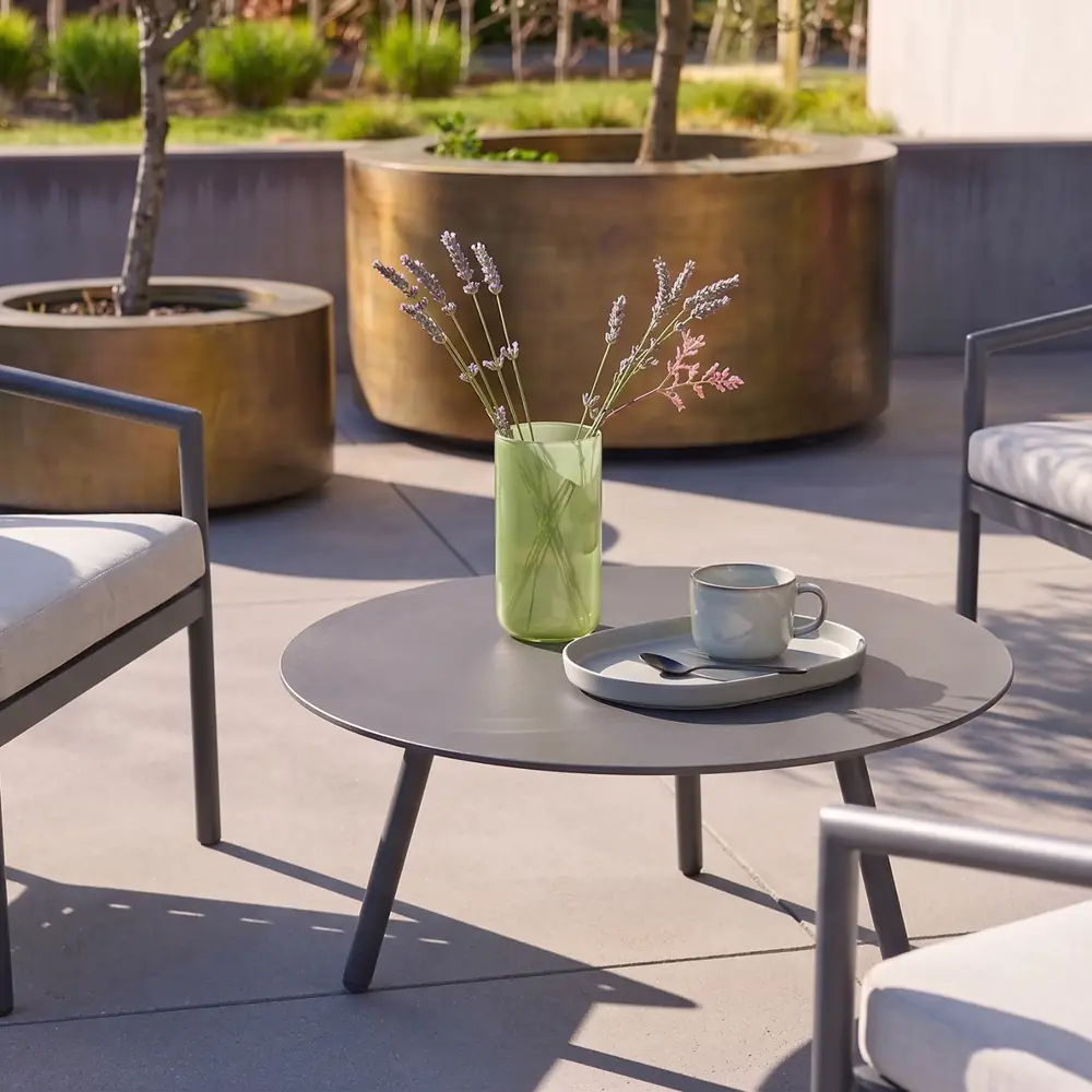 Conjunto de jardín de aluminio y cuerdas gris para 4 personas con mesa redonda: la mesa baja redonda con una taza y un jarrón de flores
