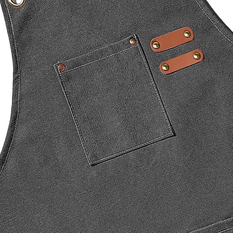 Delantal de lona de algodón negro con bolsillos y tirantes cruzados: detalle del bolsillo frontal con los remates de cuero