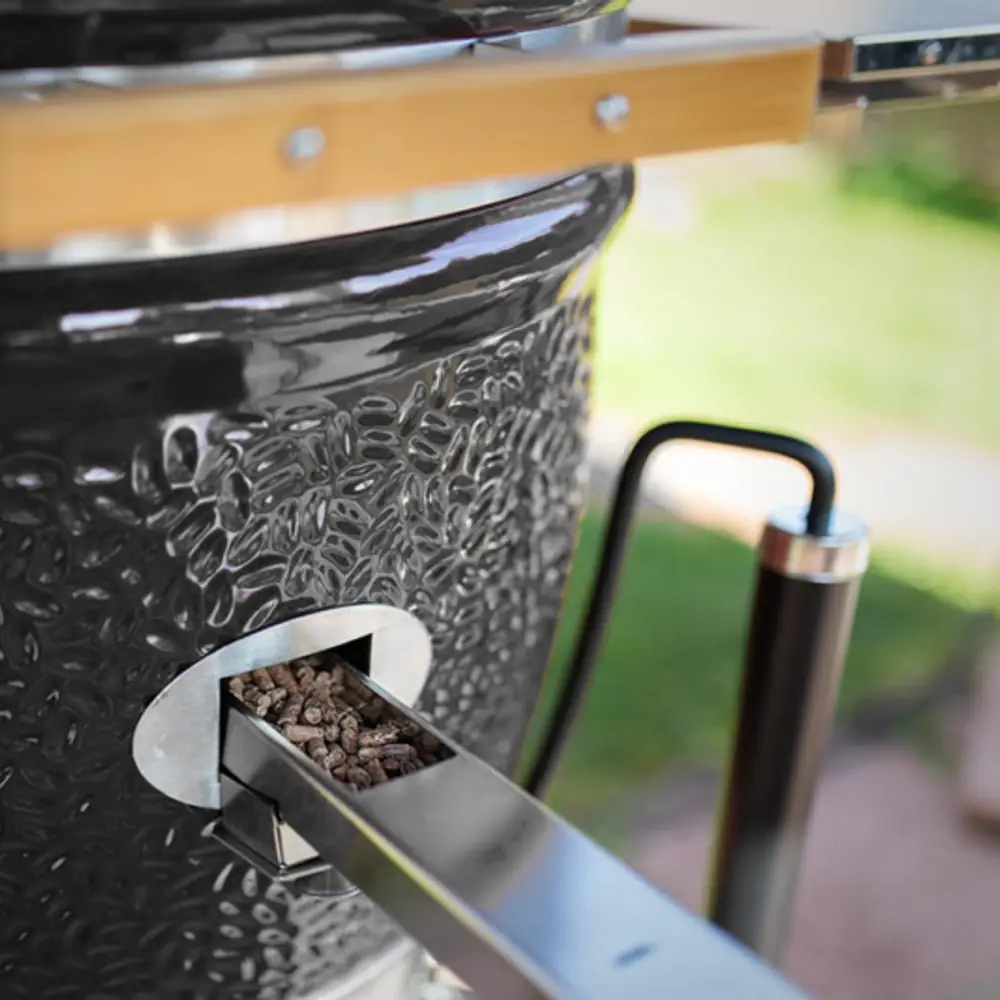 Kamado Monolith LeChef 55 cm Serie Pro 2.0 con carro y mesas de bambú: echando virutas por la entrada lateral sin abrir la tapa