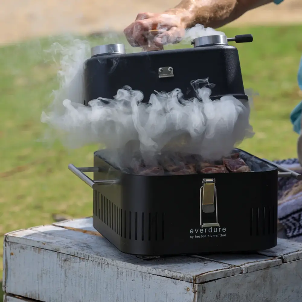 Tapa horno Everdure Cube con termómetro, para asar y ahumar: ahumando en la terraza, con el humo saliendo por la tapa