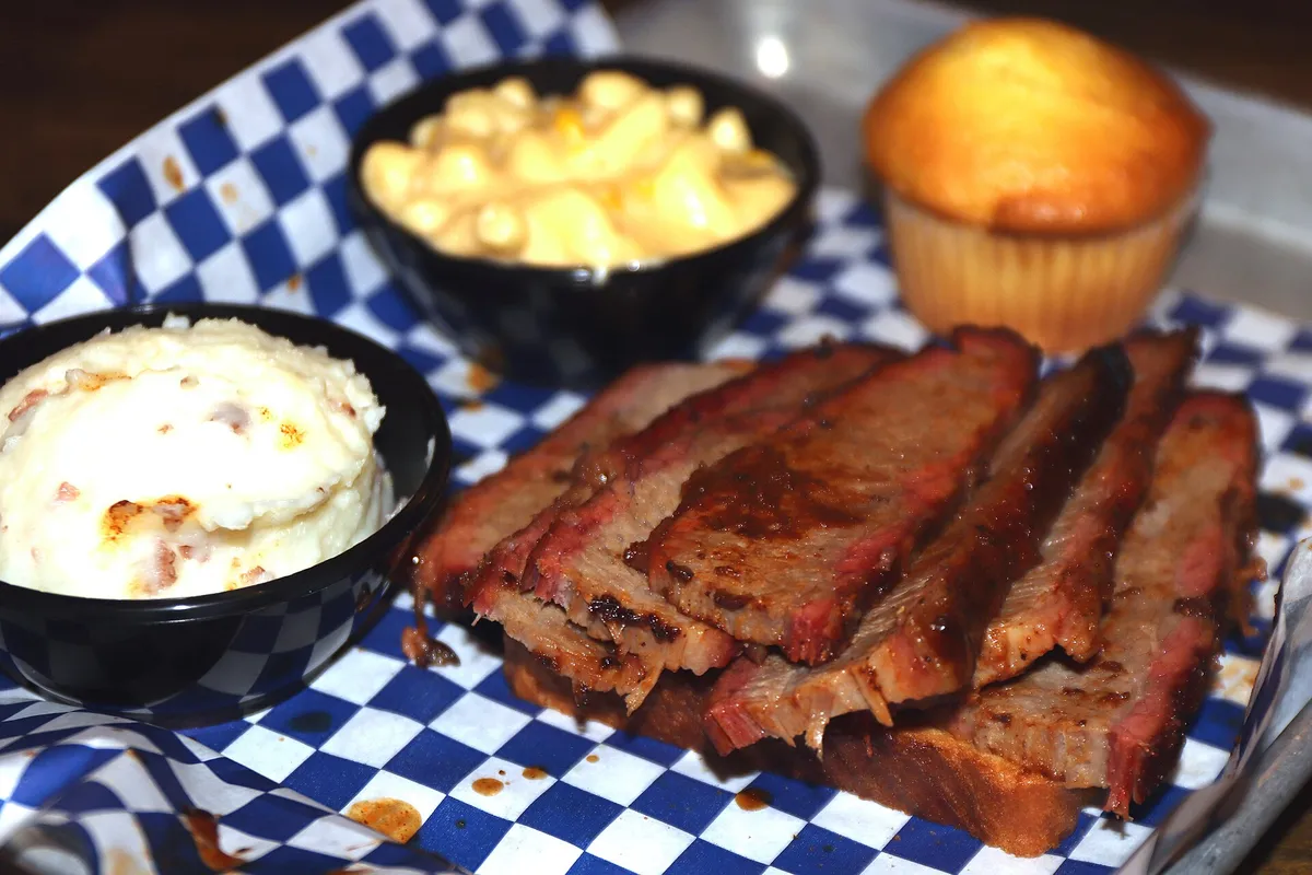 Bandeja de brisket ahumado en lonchas con macarrones con queso, puré de patata y pan de maíz al estilo de Texas