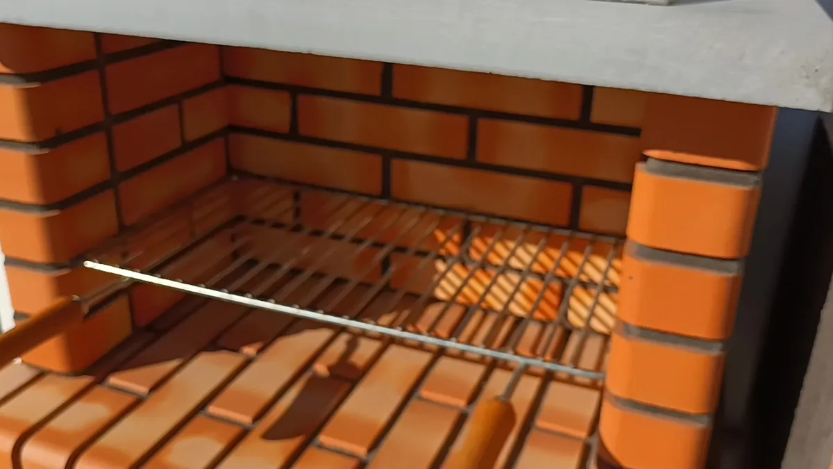 Interior de una barbacoa de obra con el hogar de ladrillo refractario y la parrilla de varillas
