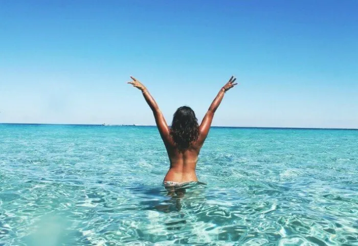 Mujer con los brazos en alto bañándose en un mar turquesa en pleno verano