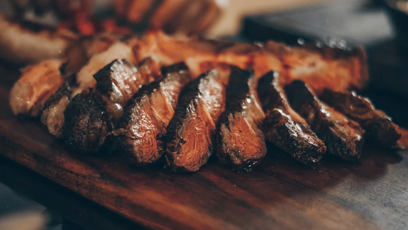 Picanha a la brasa cortada en lonchas sobre una tabla de madera, con el interior rosado y el borde tostado