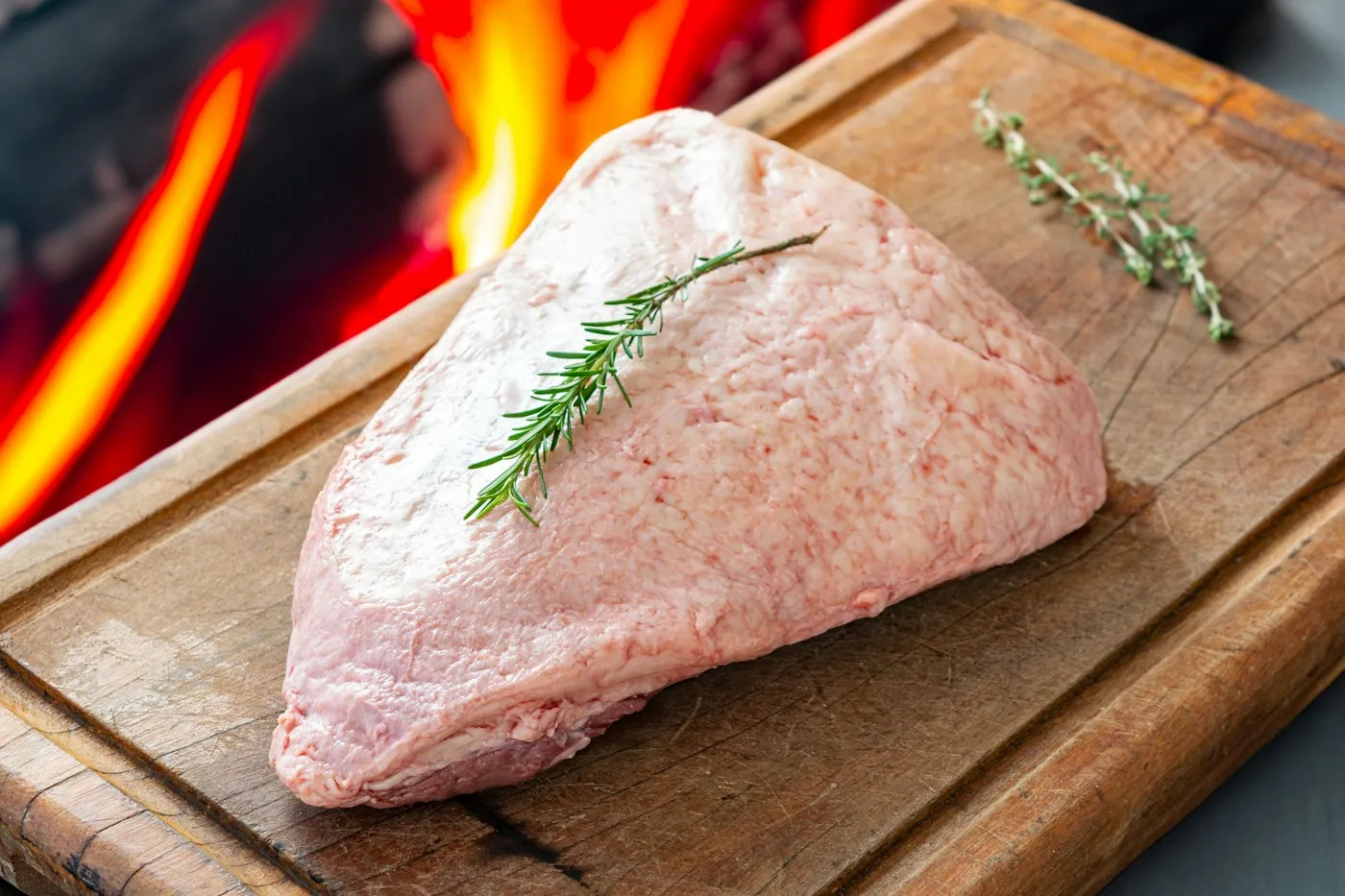 Picanha cruda entera sobre una tabla de madera, con la capa de grasa blanca por encima y una ramita de romero