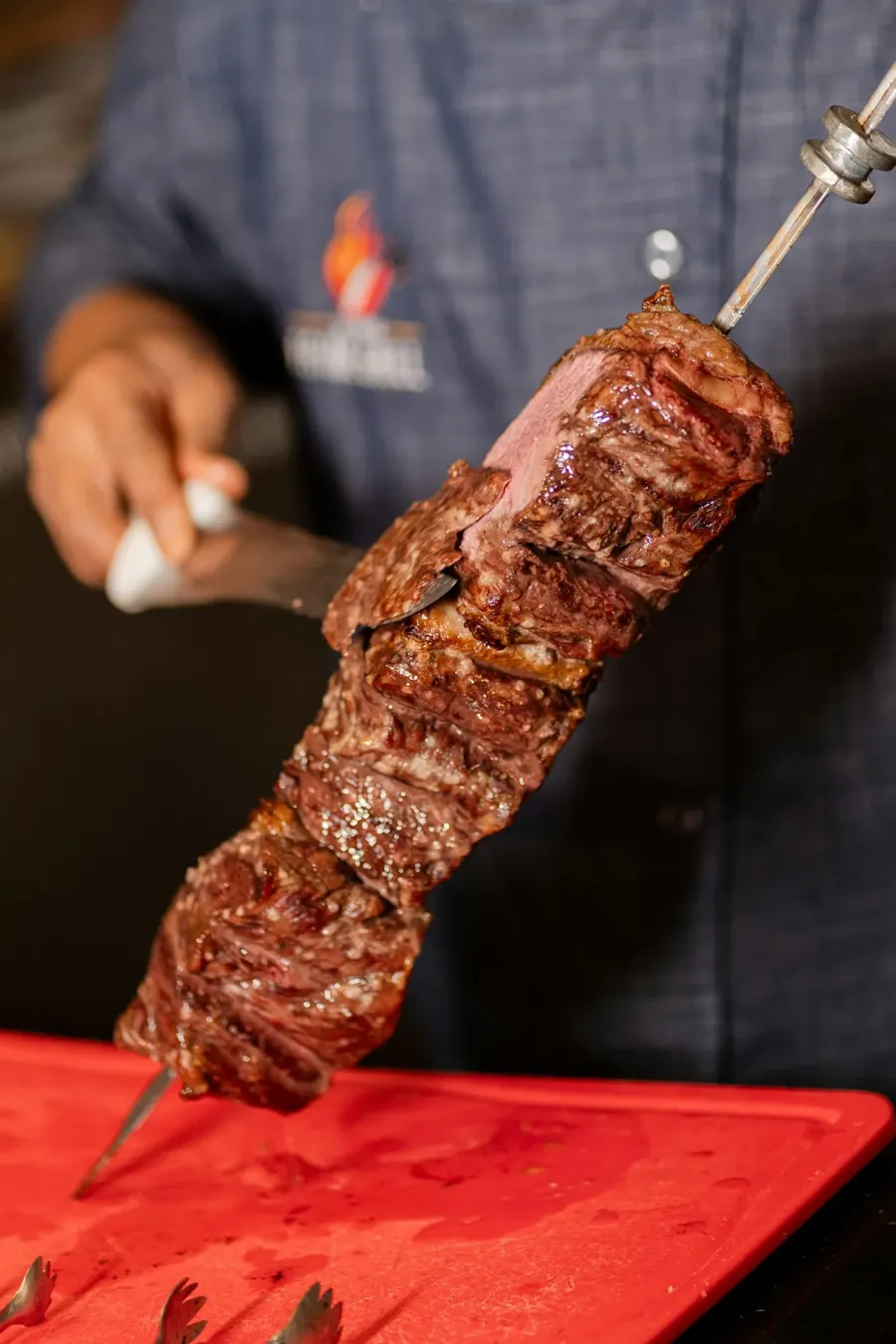 Picanha doblada en un espeto de churrasquería mientras se corta una loncha fina, con la grasa dorada y la carne jugosa