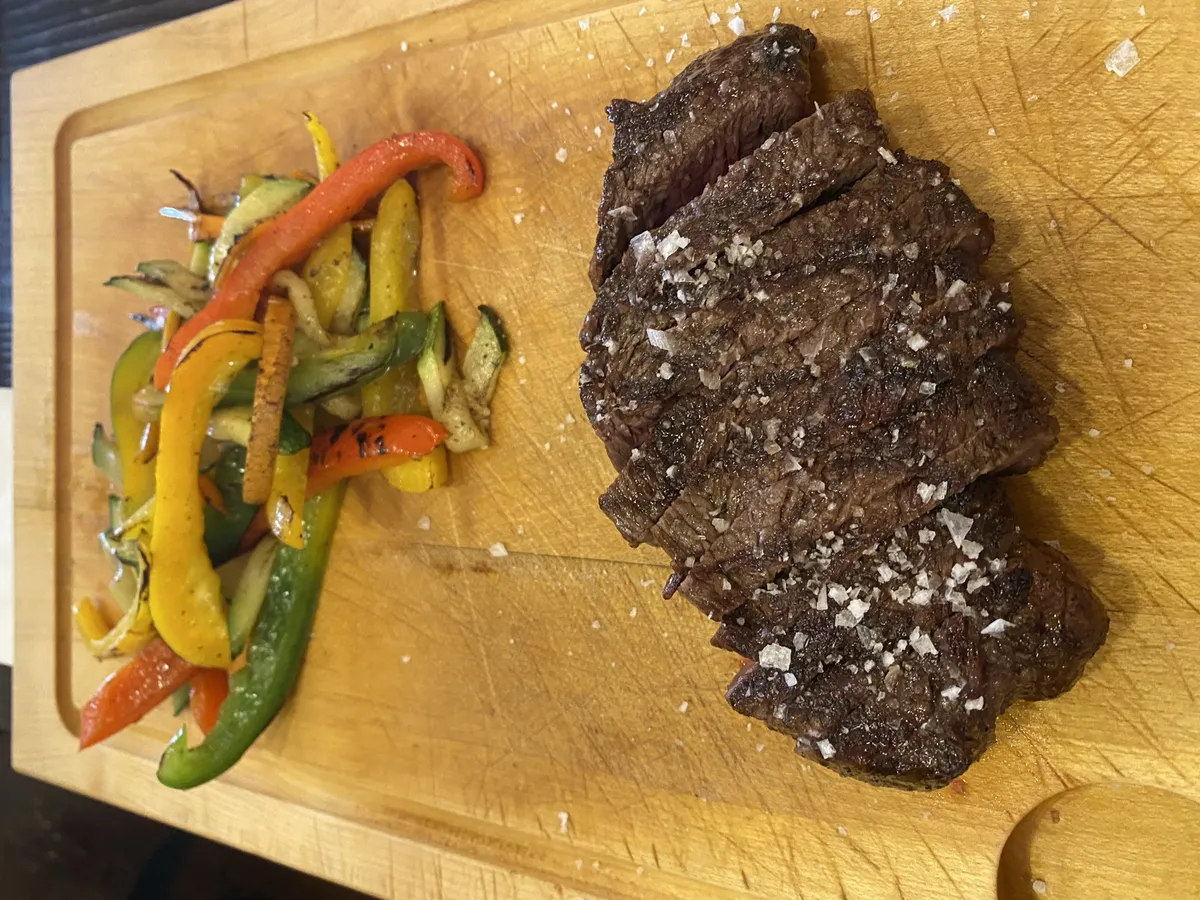 Bistec de ternera a la plancha con sal en escamas y verduras salteadas sobre una tabla de madera