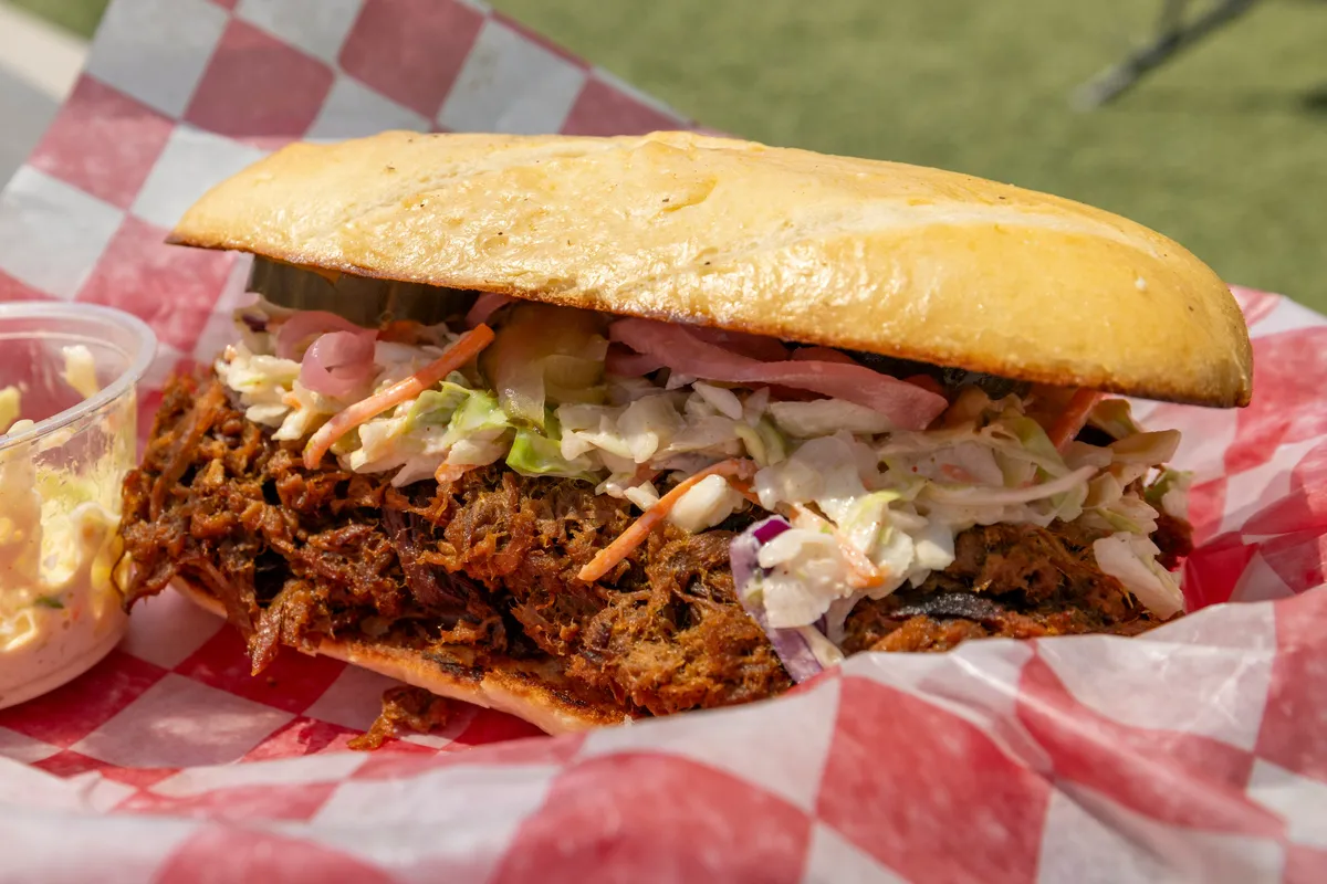 Bocadillo de pulled pork con ensalada de col y cebolla encurtida sobre un mantel de cuadros rojos