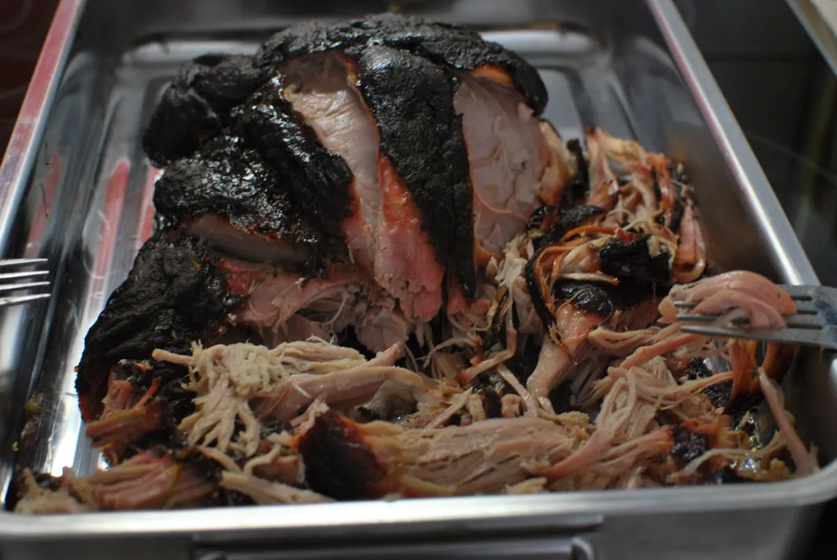 Desmechando con dos tenedores una paleta de cerdo ahumada para hacer pulled pork