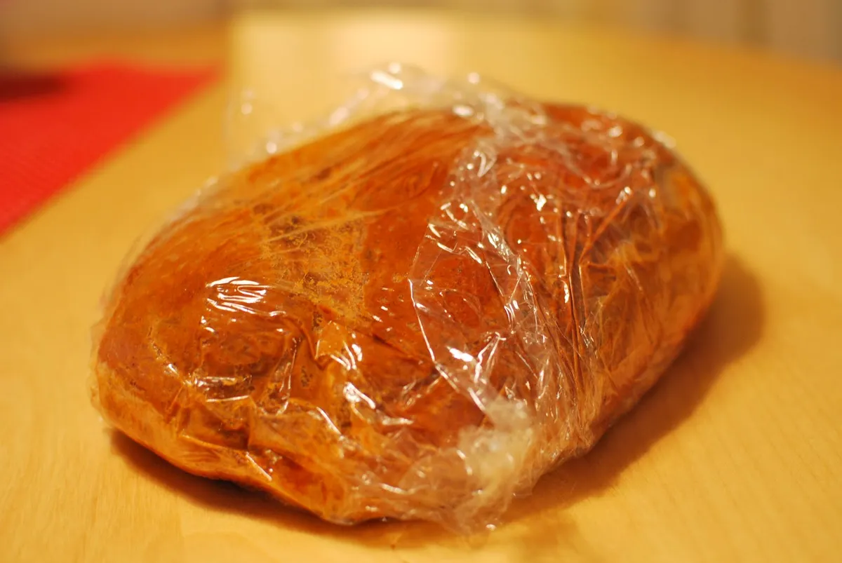Paleta de cerdo cruda untada con adobo seco de pimentón y envuelta en film transparente para pulled pork